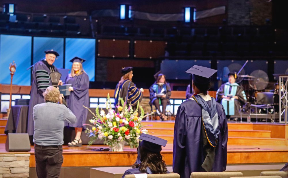 Graduate standing up with president and another graduate posing for a photo