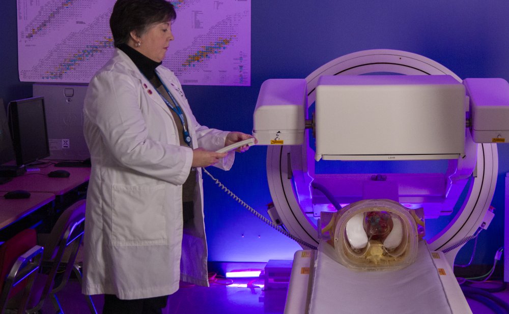 Instructor demonstrates nuclear medicine imaging equipment in a lab with purple lighting.