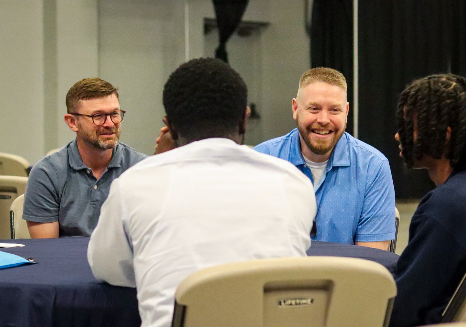 Two men in conversation at a round table during the Future Men in Healthcare Networking Event, smiling and engaged with students.