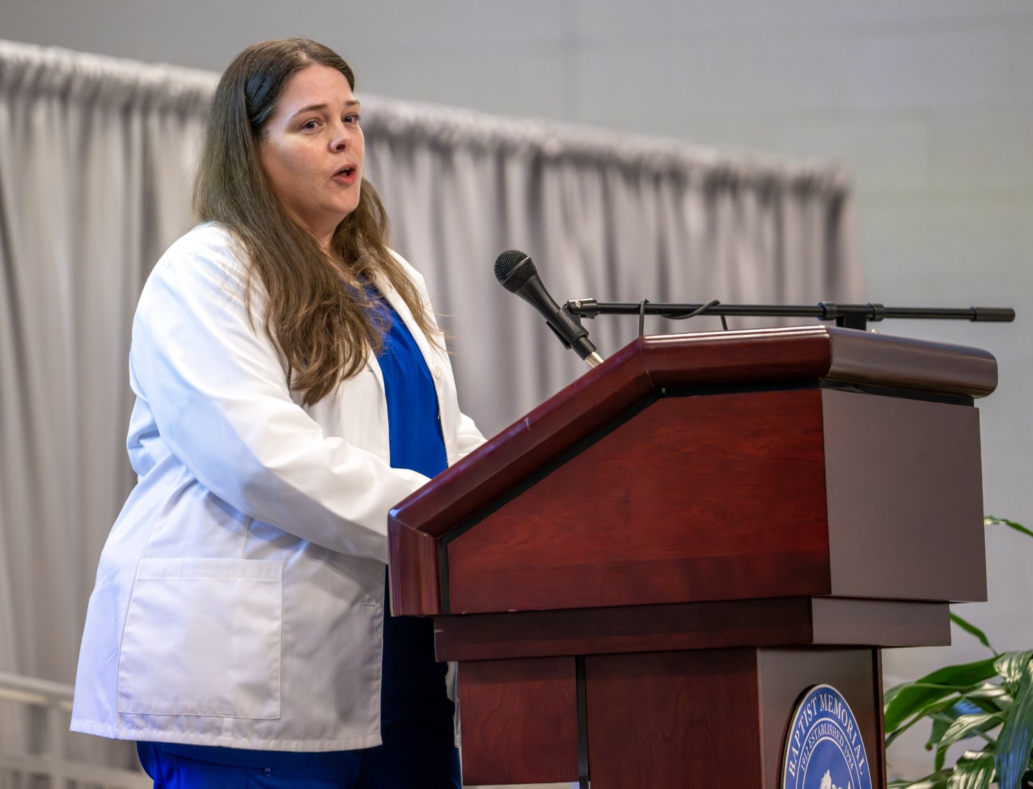 Diagnostic Medical Sonography senior student Adair Olsen speaks at the podium during the Allied Health White Coat Ceremony, wearing her white coat and addressing classmates, faculty, and guests.