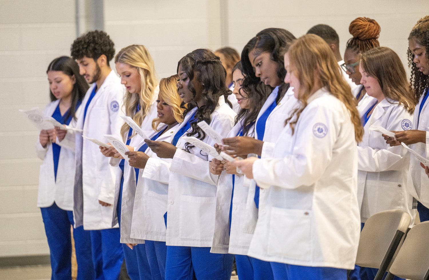 Allied Health students stand together wearing their white coats and blue scrubs as they recite the professional oath during the White Coat Ceremony at Baptist Health Sciences University.