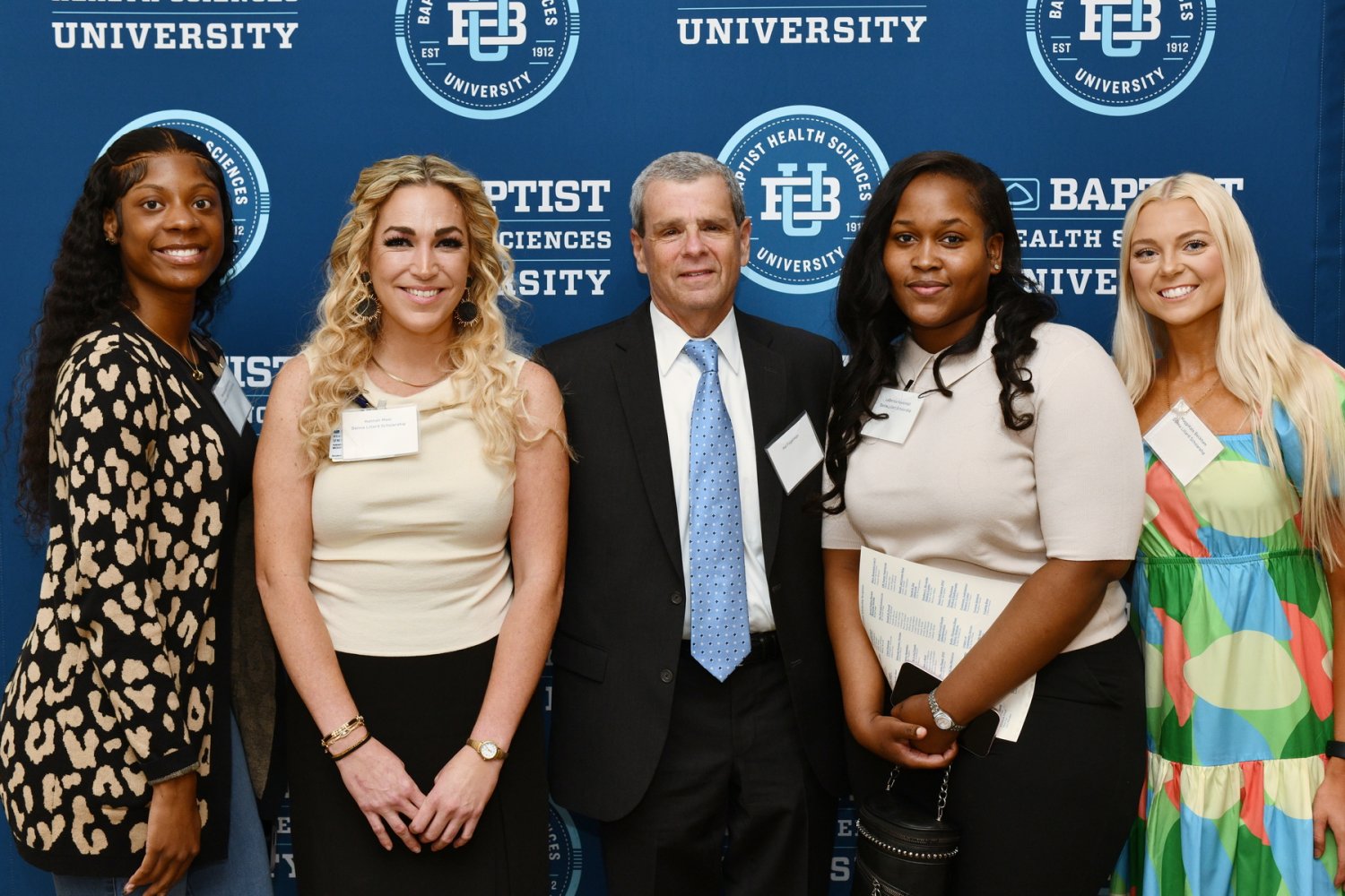 A man and four women pose together in front of a Baptist Health Sciences University step-and-repeat banner.
