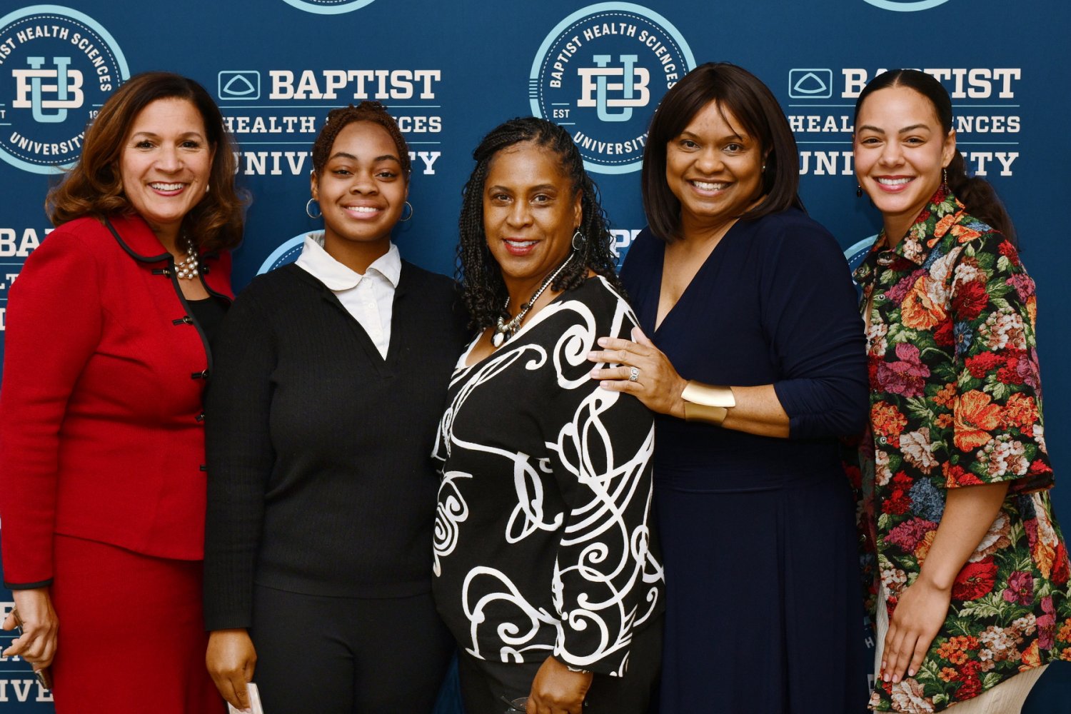 Five women stand and smile together in front of a Baptist Health Sciences University backdrop.
