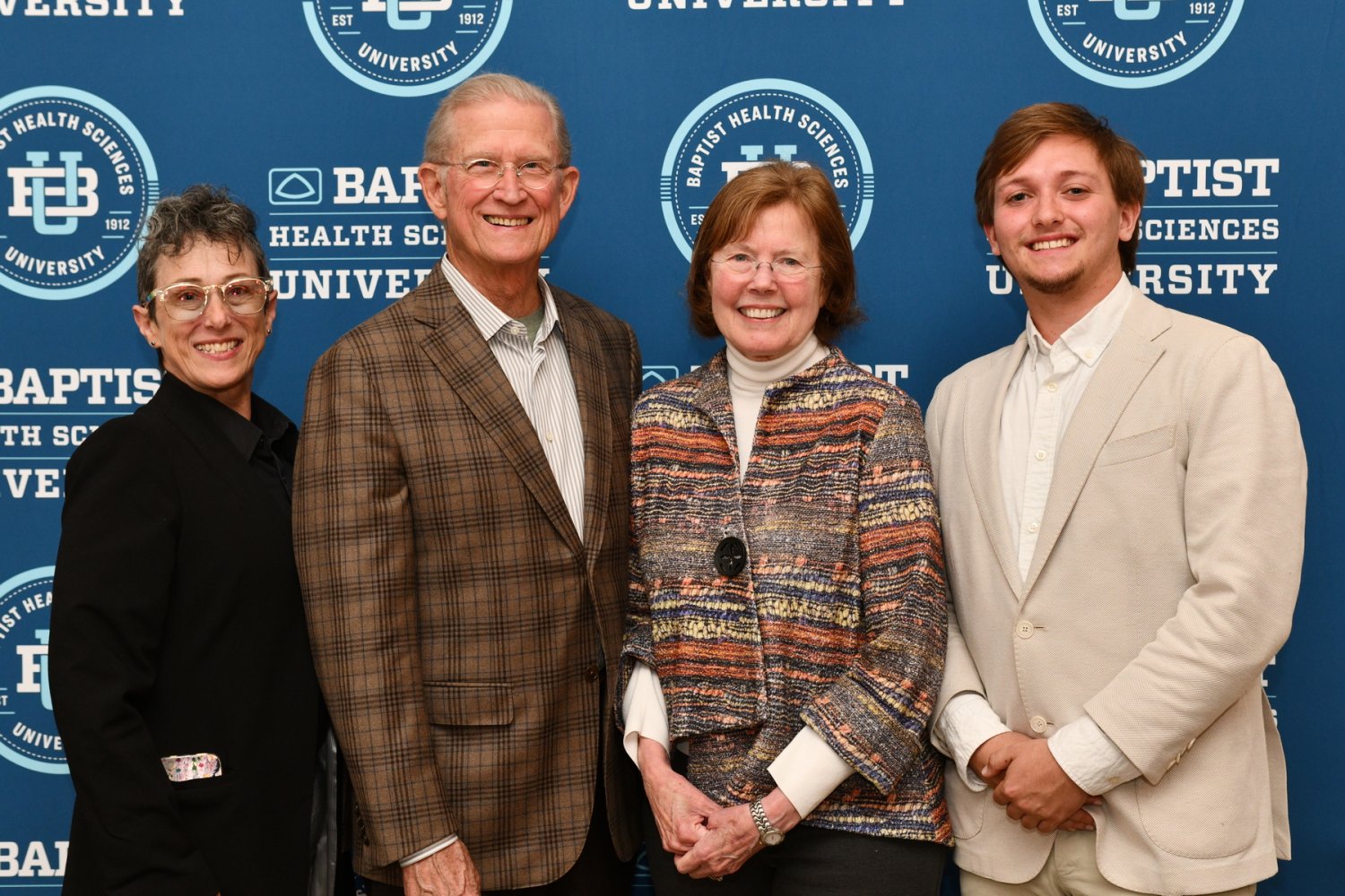 Four people stand side by side smiling in front of a Baptist Health Sciences University backdrop.