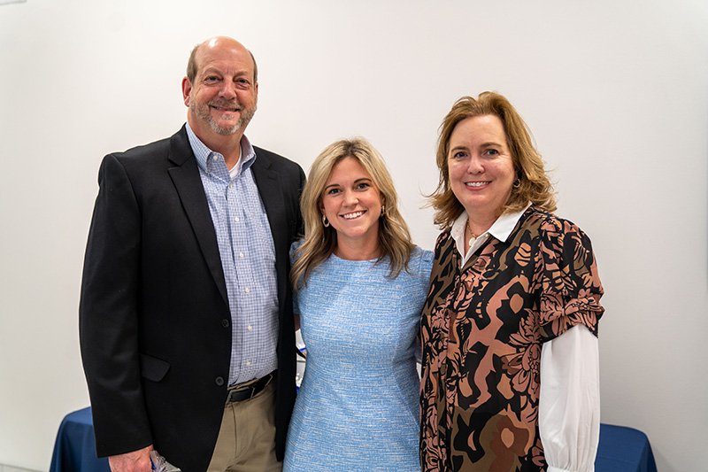 three individuals smiling with a white wall in the background