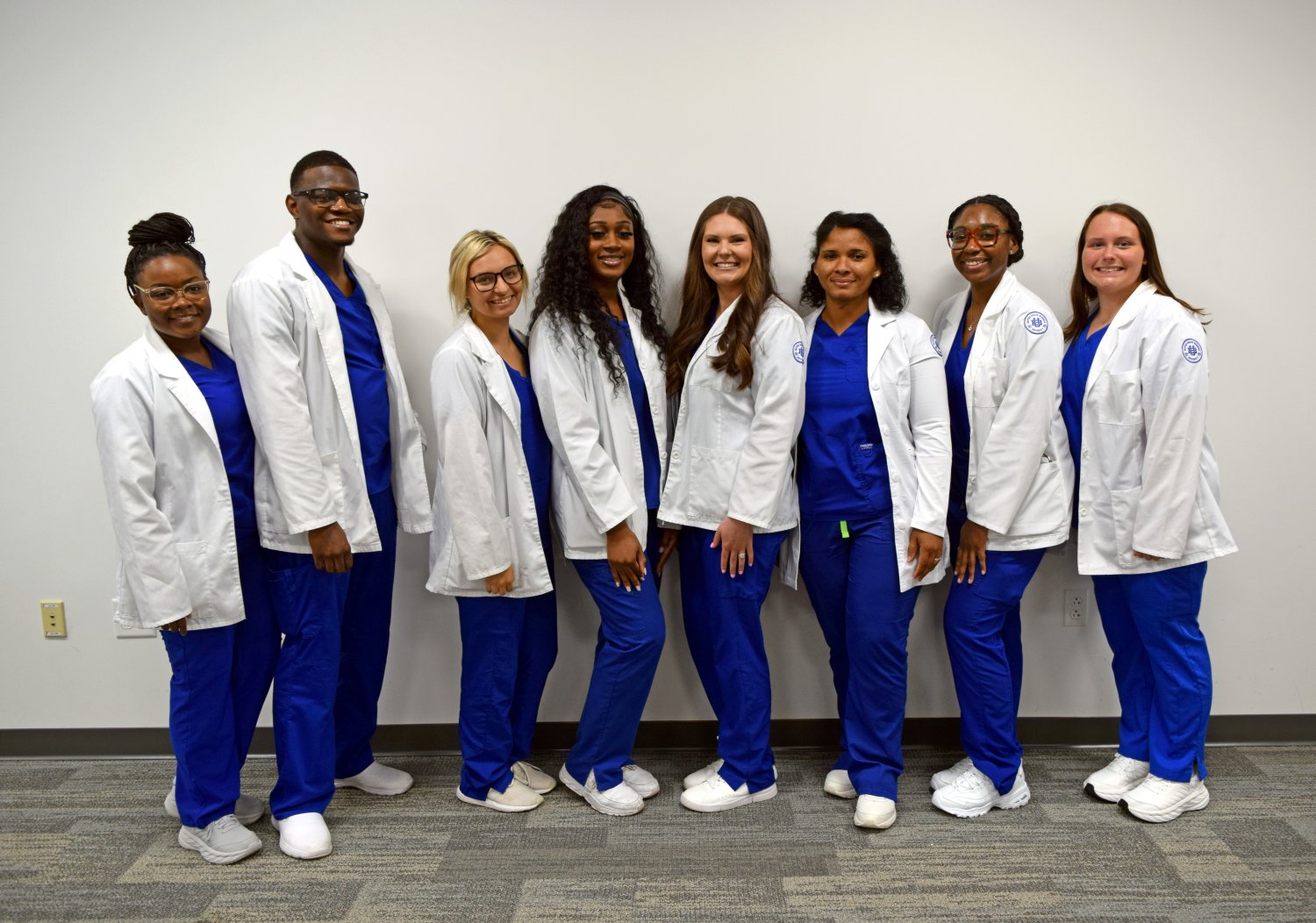 group of students in blue scrubs and white coats standing in front of a blank wall