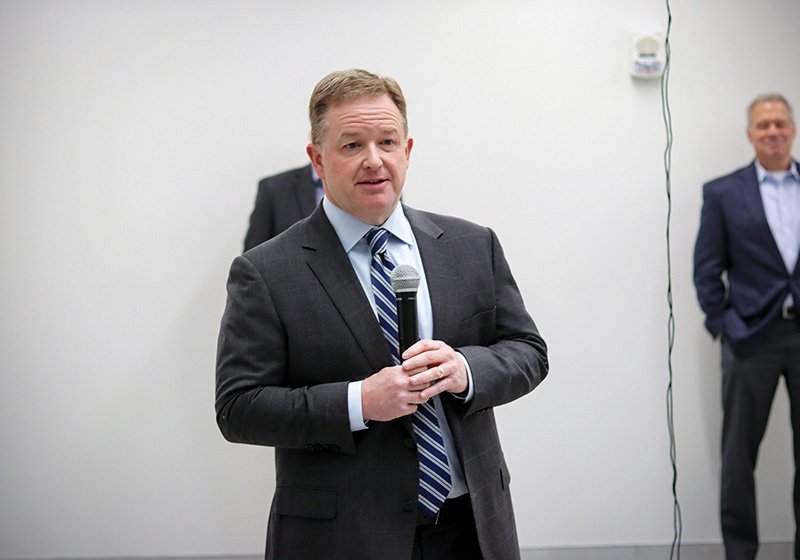 Jason Little speaking to the crowd with two individuals standing behind him