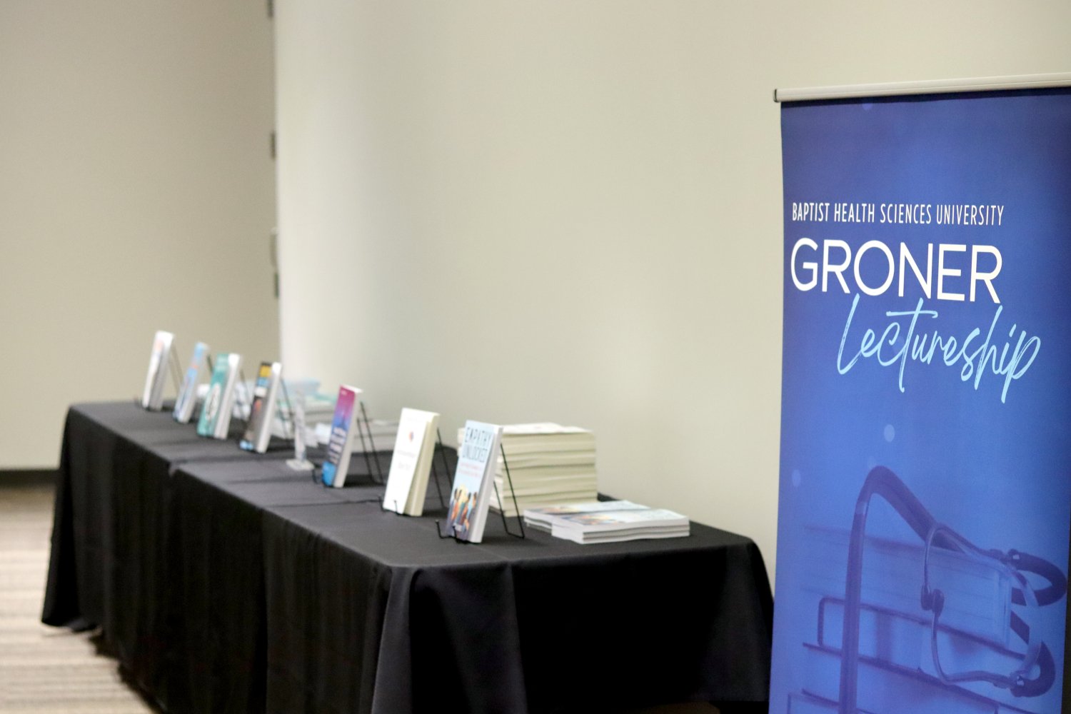 books standing on a black table and a blue screen with the words groner lectureship written on it 