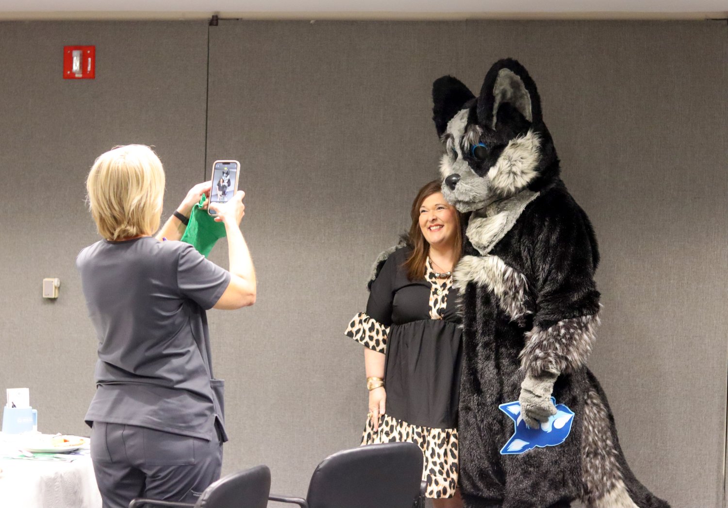 A woman smiles as she poses with the Baptist mascot, Hartley, while another woman takes their photo using a smartphone at a lunch-and-learn event.