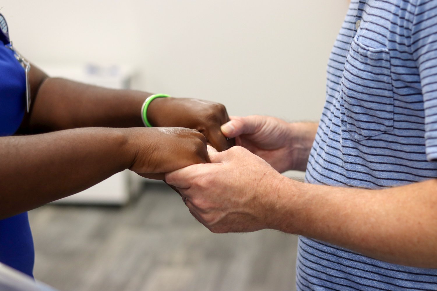 A man and a student in blue scrubs clasp hands during a heartfelt moment in a ceremonial setting.
