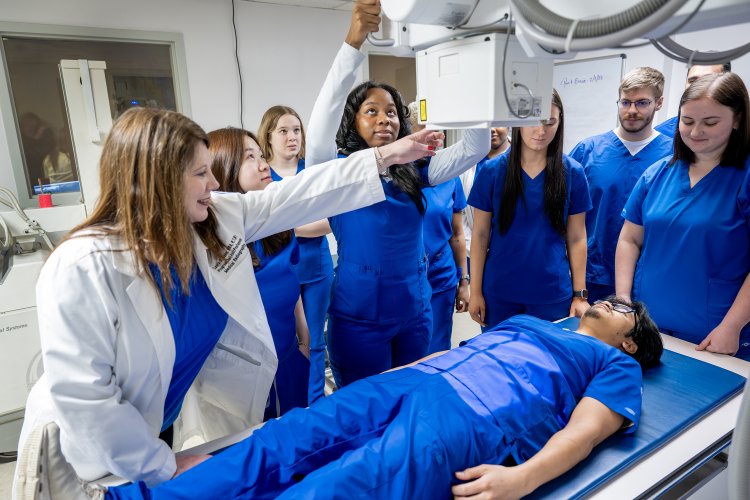 Radiography students observe as an instructor demonstrates X-ray positioning on a classmate during hands-on lab training.