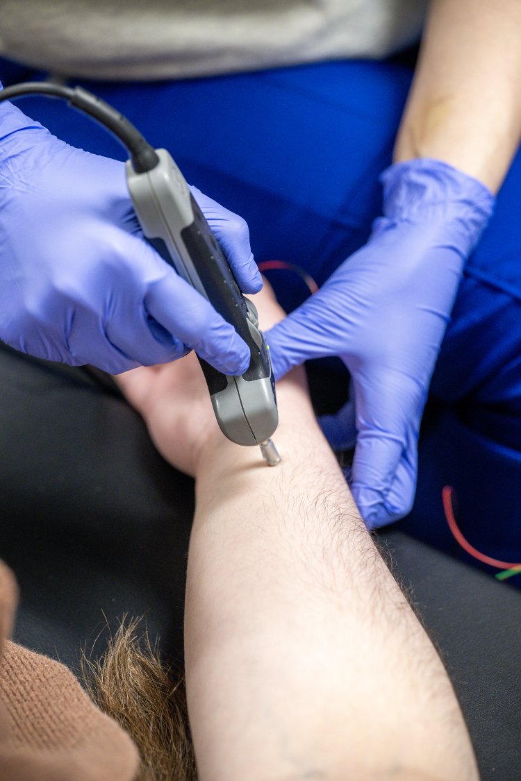A student operates ultrasonic testing equipment in an NDT lab while reviewing inspection data on a laptop.