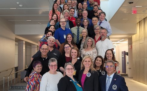A large group of osteopathic medical educators and leaders pose together on a wide staircase at the ECOP/OPP meeting in Des Moines. The group includes men and women standing in several rows, smiling toward the camera.