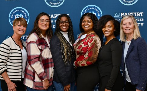 Group of six people smiling in front of a Baptist Health Sciences University backdrop.