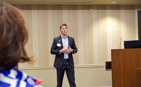 Brian Welton, CEO of Baptist North Mississippi, speaks to attendees during the Lunch and Learn event, standing in front of a podium in a warmly lit conference room.