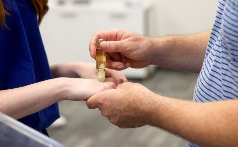 A close-up of a man's hands anointing a student's hand with oil from a small glass vial during a blessing ceremony.