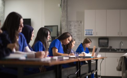 Students in blue scrubs take notes during a classroom session at Baptist Health Sciences University.